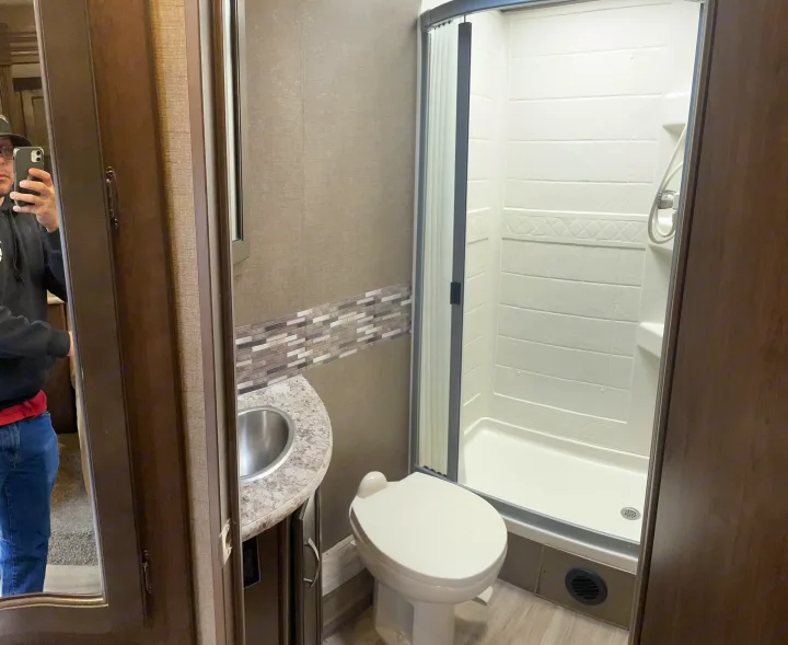 Clean RV rental bathroom featuring a toilet, compact sink vanity, and bright shower with sliding glass door.. Thor Motor Coach Freedom Elite 2019