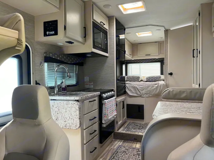 Spacious RV rental interior featuring a modern kitchen with sink and stove, cozy bedroom, and comfortable dinette.. Thor Freedom Elite 2022