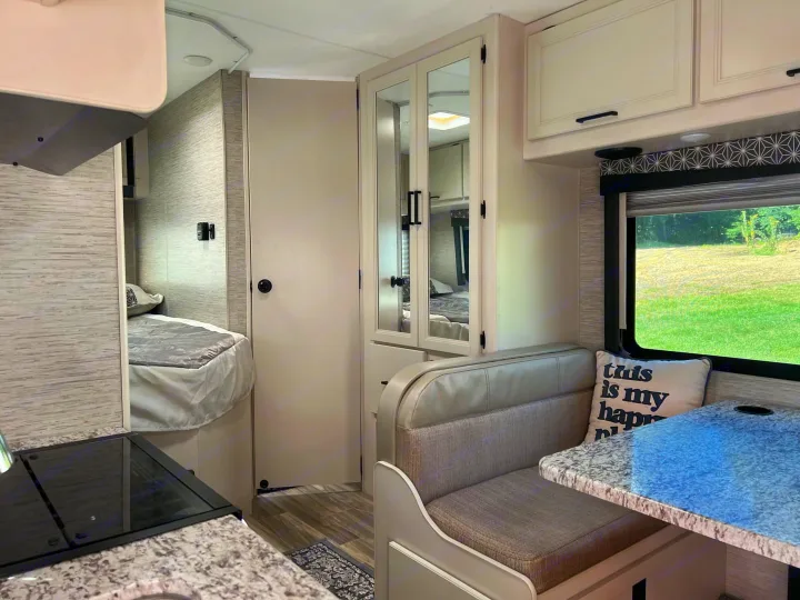 Inside a bright rv rental, showcasing the kitchen, dinette, and a glimpse of the bedroom. Neutral tones & ample space.. Thor Freedom Elite 2022