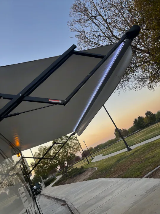 Enjoy the illuminated awning of this Greyhawk RV rental at dusk, parked beside a scenic park with paths and trees.. Jayco Greyhawk 2020