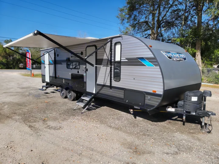 This sleek grey travel trailer, ideal for RV rental, boasts an extended awning on a sunny gravel lot. Perfect for camping adventures.. Forest River Salem Cruise Lite 2020