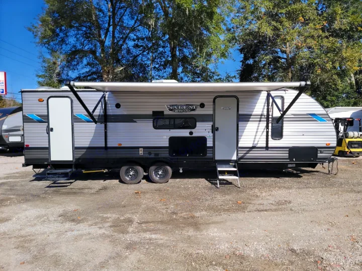 Grey travel trailer for RV rental, featuring a deployed awning and two entry doors. Parked on gravel, ready for adventure.. Forest River Salem Cruise Lite 2020