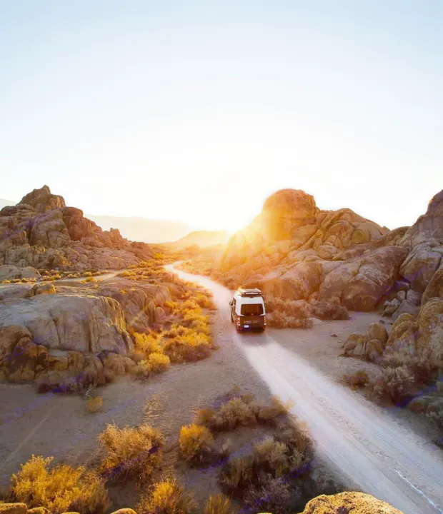 Embrace the journey! This rv rental camper van drives a winding desert road through rocky hills at golden hour.. Mercedes-Benz Sprinter 2017