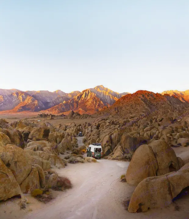An RV rental camper van travels a dirt road through a rocky desert, mountains glowing at sunset. Perfect for an outdoor road trip.. Mercedes-Benz Sprinter 2017