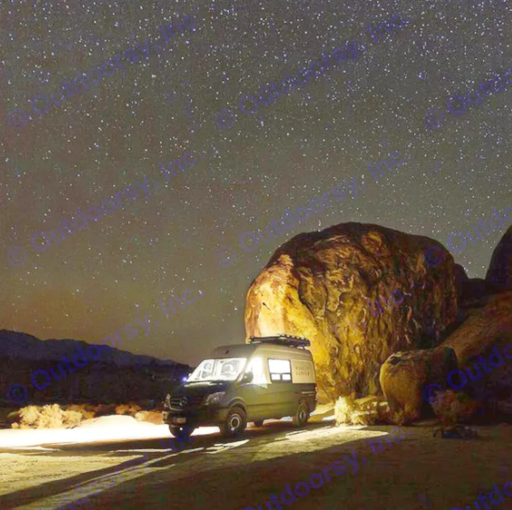An RV rental camper van glows under a brilliant night sky full of stars, parked by massive rocks for a perfect night camping adventure.. Mercedes-Benz Sprinter 2017