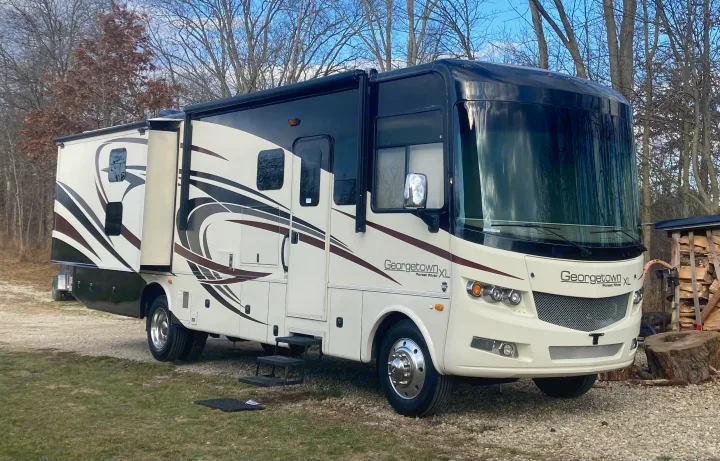 A large white and black Georgetown XL rv rental motorhome with slide-outs extended, parked on a gravel drive with trees.. Georgetown XL 2015