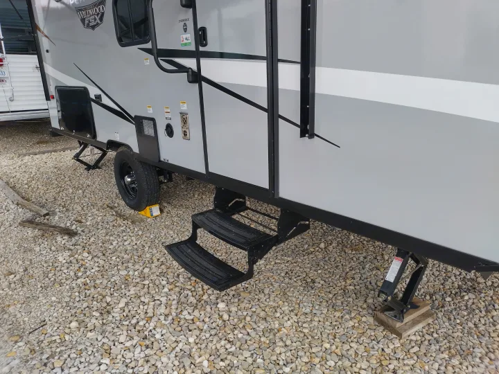Close-up of a grey RV rental travel trailer on gravel, showing steps, tire, and stabilizer jacks on wood blocks.. Forest River Other 2022