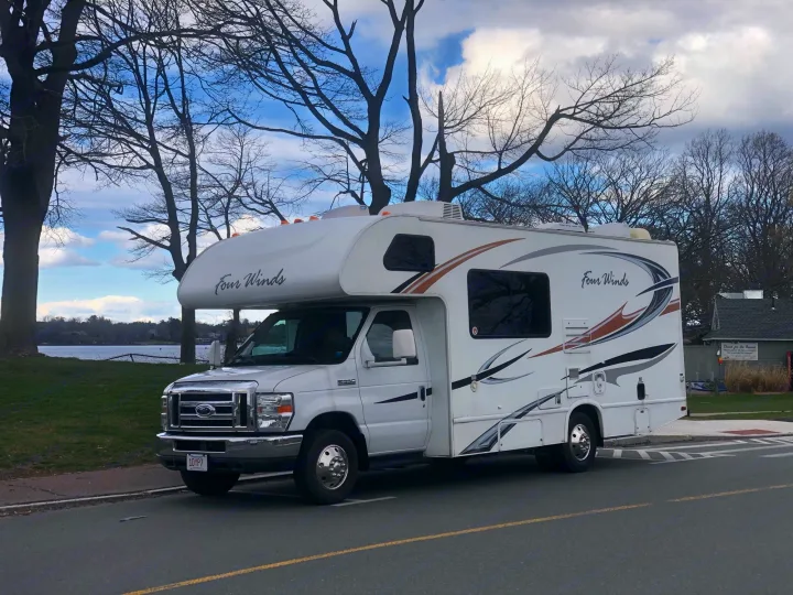 White Four Winds Class C RV rental parked roadside. This motorhome is by water, bare trees, and a cloudy sky.. Four Winds Four Winds Motorhome 2011