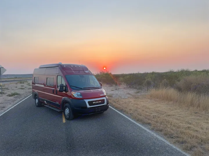 A vibrant red RV rental parked on a quiet road at sunset, casting warm light on the dry landscape. Ideal for a scenic road trip.. Solis 59P Solis 2022