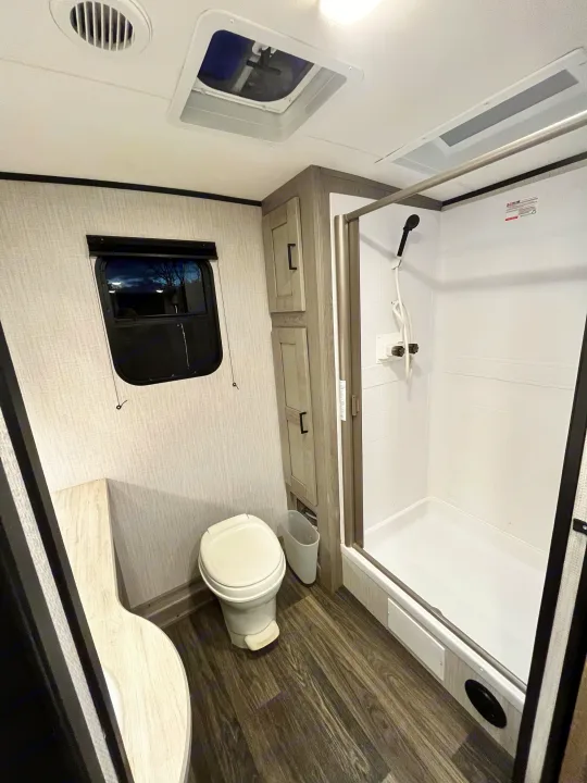 This RV rental bathroom offers comfort on the go: a compact toilet, standing shower, cabinet storage, window, and wood-look floor.. Heartland RVs Mallard 2021
