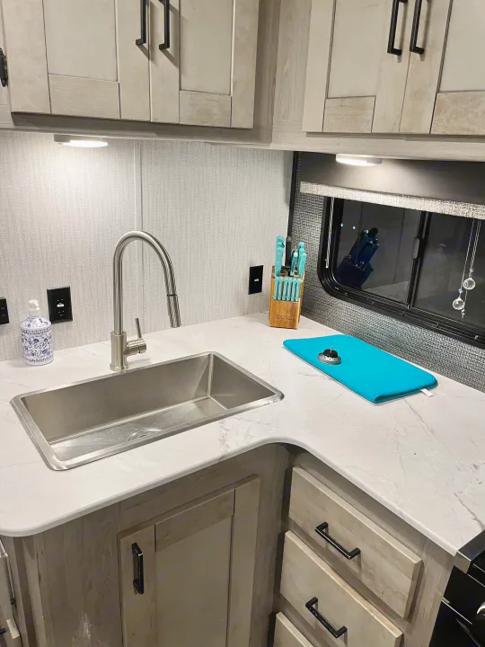 Modern RV rental kitchen with a stainless steel sink, sleek faucet, white marble counters, and light wood cabinets.. Heartland RVs Mallard 2021