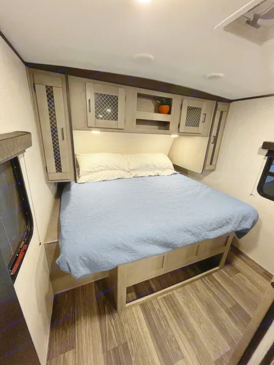 Spacious RV rental bedroom with a comfy queen bed, built-in storage, under-bed space, and wood floors.. Heartland RVs Mallard 2021