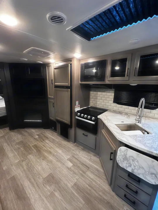 Inside a modern RV rental: well-equipped kitchen, living area with TV & fireplace, and comfy sleeping space.. Jayco White Hawk 2022