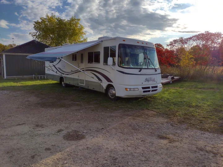 White and green DayBreak RV rental with awning extended, parked on gravel amidst autumn trees and blue sky.. Damon Corporation Daybreak 2001