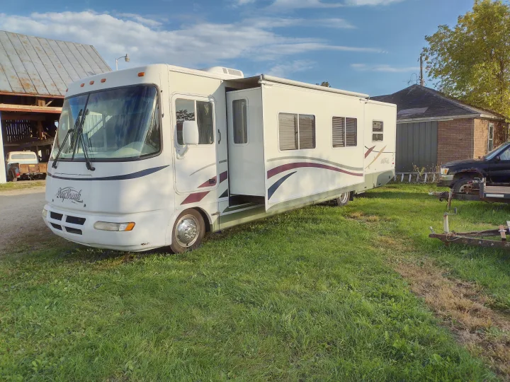 This large white RV rental, with its side slide-outs extended, is parked on green grass under a clear blue sky.. Damon Corporation Daybreak 2001