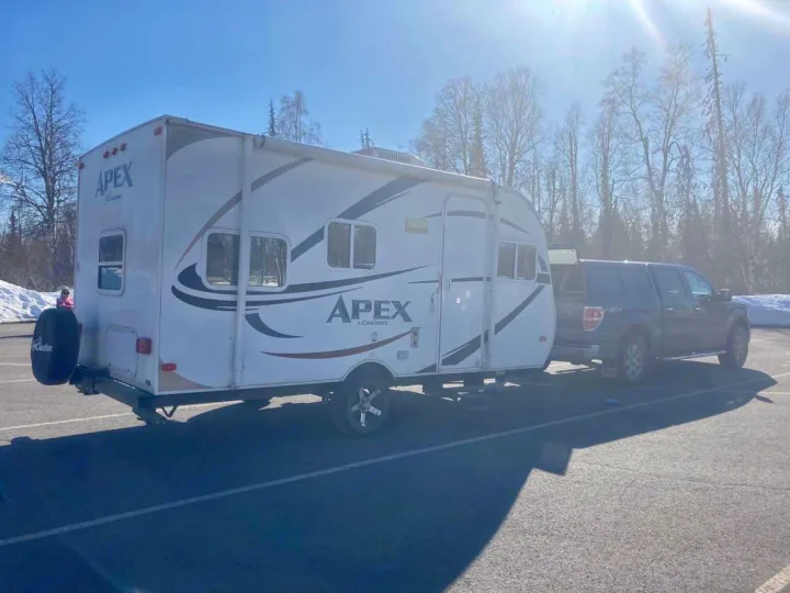 This Apex RV rental, a travel trailer, is hitched to a pickup truck in a sunny outdoor setting, ready for your road trip.. Coachmen Apex 2012