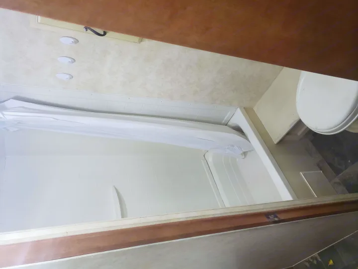 View of an RV rental bathroom featuring a white shower with curtain, overhead lights, and a partial view of the toilet.. Coachmen Apex 2012