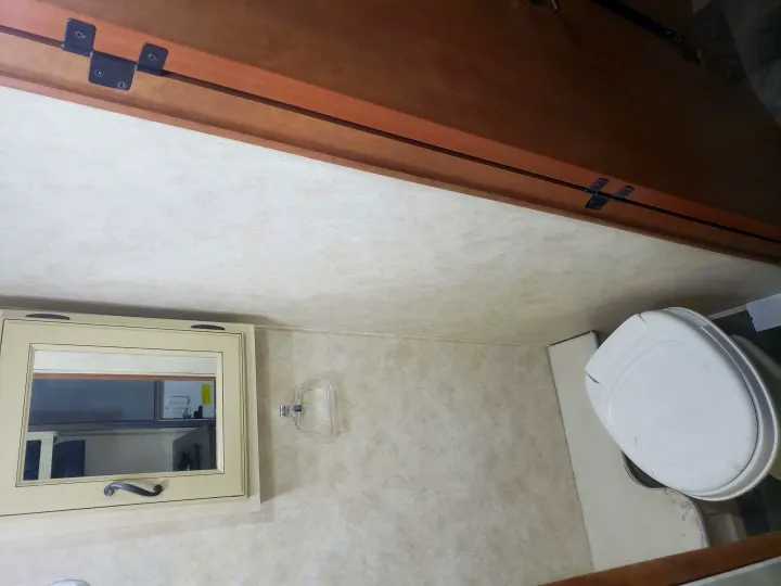 RV rental bathroom: Compact space with a toilet, mirrored cabinet, and upper wooden cabinetry.. Coachmen Apex 2012