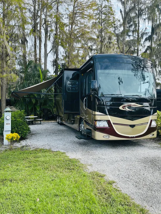 Spacious RV rental parked at site 404 in a scenic campground, surrounded by moss-draped trees and an extended awning.. Fleetwood Discovery 2011