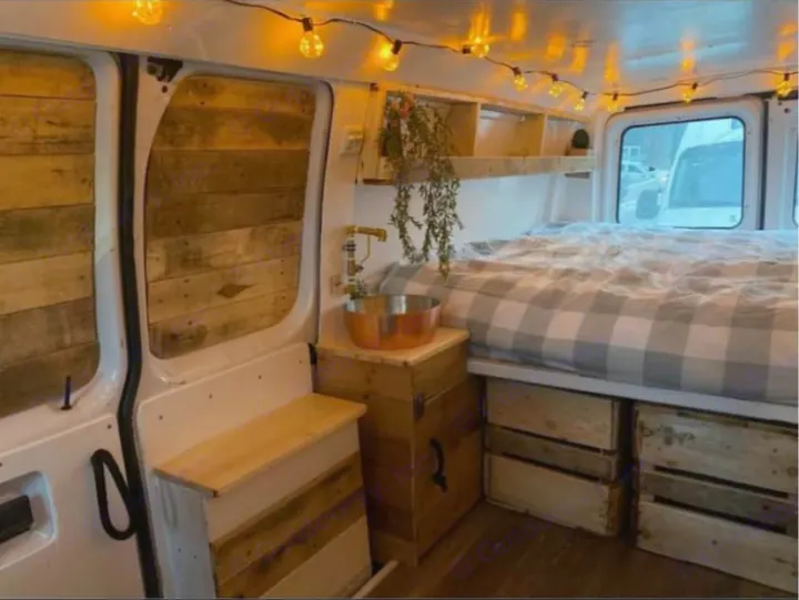 Inside an RV rental: a cozy, custom camper van with reclaimed wood paneling, plaid bed, string lights, and compact sink.. Ford Econoline 2012