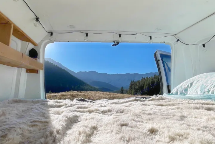 Cozy rv rental interior with a fluffy bed and string lights, looking out at a serene mountain and forest landscape.. Ford Econoline 2012