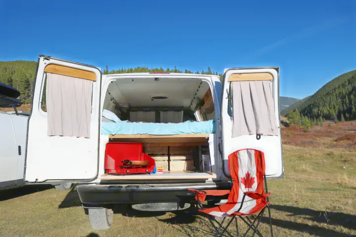 This rv rental features an open camper van's interior: bed, stove, & Canadian chair in a scenic outdoor setting.. Ford Econoline 2012