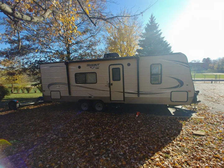 A beige travel trailer, an RV rental, is parked outdoors amidst golden autumn leaves under a bright blue sky.. Keystone RV Hideout LHS 2017