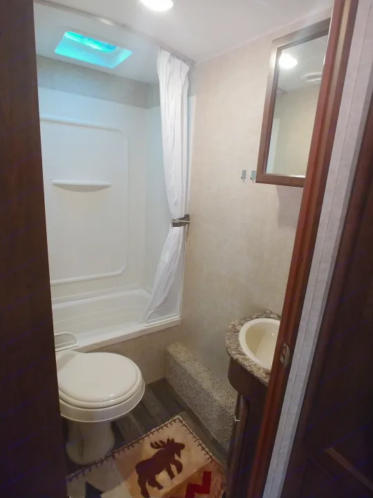 Compact bathroom in an RV rental with a shower, toilet, sink, skylight, and a cozy moose-themed rug.. Keystone RV Hideout LHS 2017