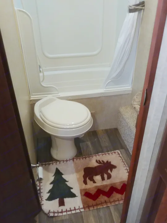 Inside an RV rental: a compact bathroom with a toilet, stand-up shower, and rustic-themed floor mat.. Keystone RV Hideout LHS 2017