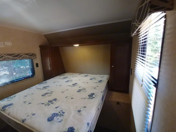 RV rental bedroom interior: Features a bed with floral mattress, windows, and built-in storage cabinets.. Keystone RV Hideout LHS 2017