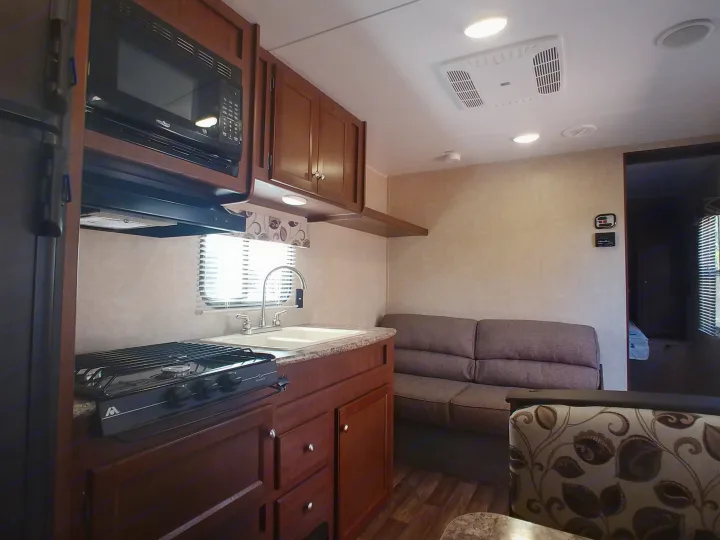 Cozy RV rental interior with a well-equipped kitchen, including a microwave, stove, and sink, plus a comfortable sofa in the living area.. Keystone RV Hideout LHS 2017