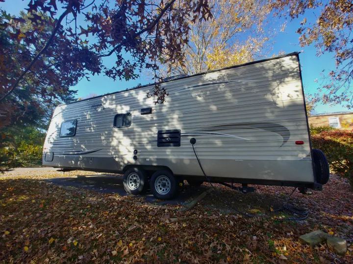 Spacious RV rental, a travel trailer, parked amidst autumn leaves and trees, ready for an outdoor getaway.. Keystone RV Hideout LHS 2017