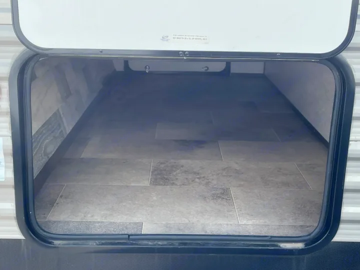 Empty pass-through storage compartment of an RV rental, featuring a tile-patterned floor.. Dutchmen Coleman Lantern LT 2022