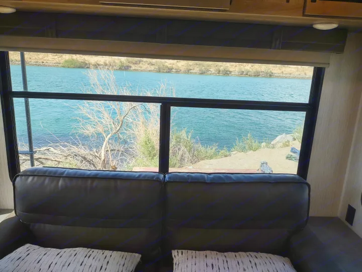An RV rental offers beautiful views: From a comfortable couch, a wide window shows a tranquil lake, dry land, and sparse trees.. Palomino Puma 31-RLQS 2022
