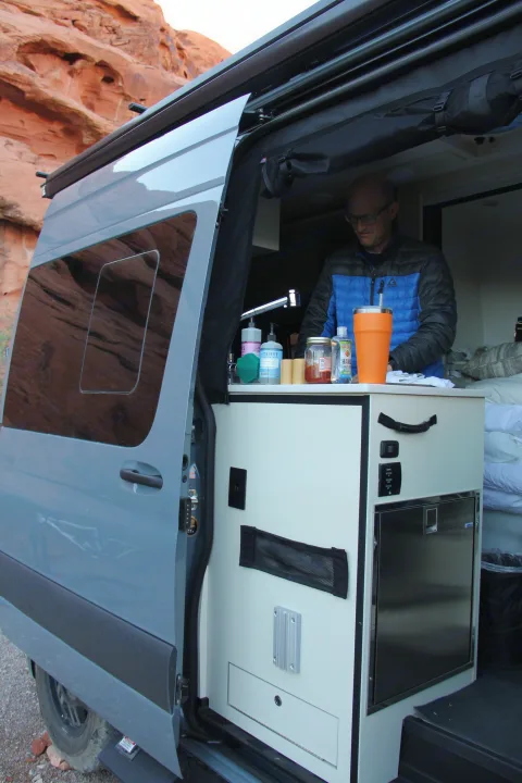 Man inside a grey **rv rental** van with an open side door, showcasing the built-in kitchen and countertop.. Mercedes Sprinter Van 2022