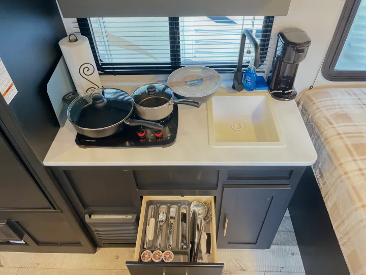 RV rental kitchen: compact counter with cooktop, sink, coffee maker, and an organized drawer of utensils and coffee pods.. Keystone RV Springdale 2022