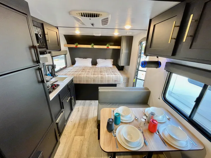 RV rental interior with a cozy bed, fully equipped kitchenette (sink, stove, microwave, fridge), and a dinette for meals.. Keystone RV Springdale 2022