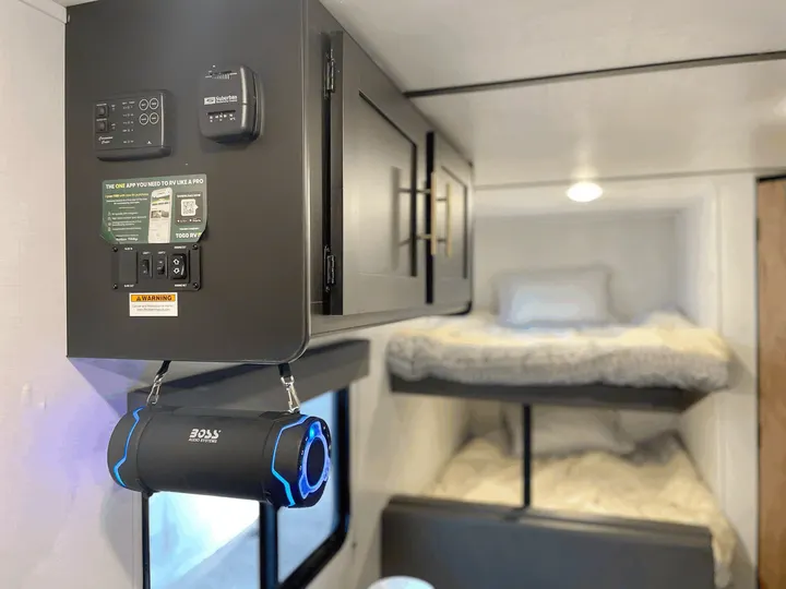 RV rental interior: control panel, thermostat, and bunk beds visible, with a hanging BOSS speaker.. Keystone RV Springdale 2022