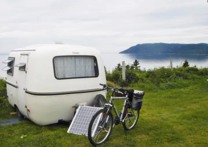Your rv rental getaway: white camper, bike, & solar panel by calm waters & mountains. Ideal for serene camping.. Boler B13 1973