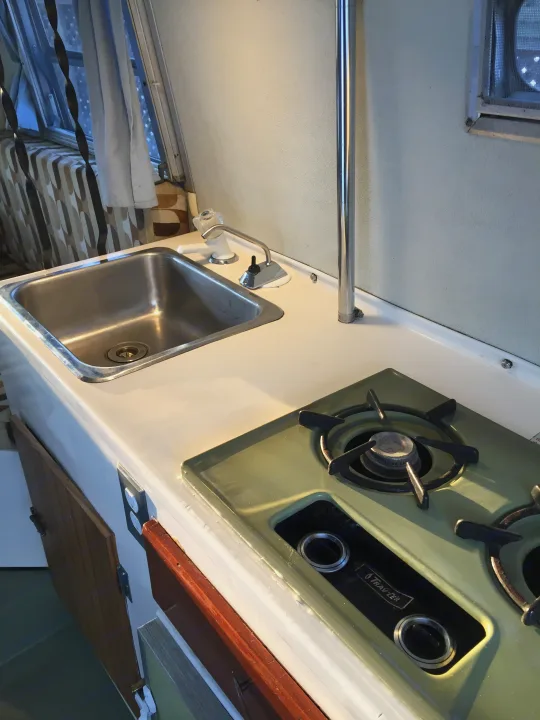Inside an RV rental: a compact kitchen area featuring a sink, faucet, and a green two-burner stovetop.. Boler B13 1973