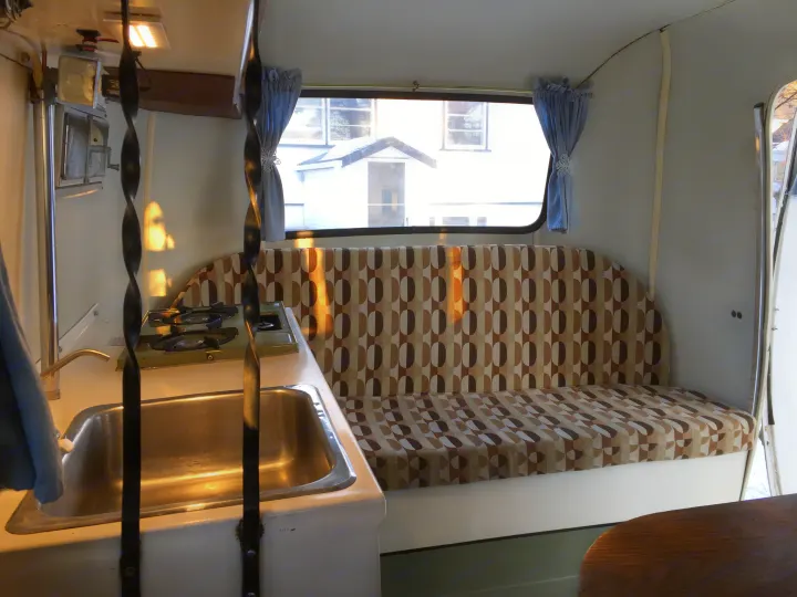 Vintage RV rental interior: kitchen with sink and stove, patterned bench seating, and bright window.. Boler B13 1973