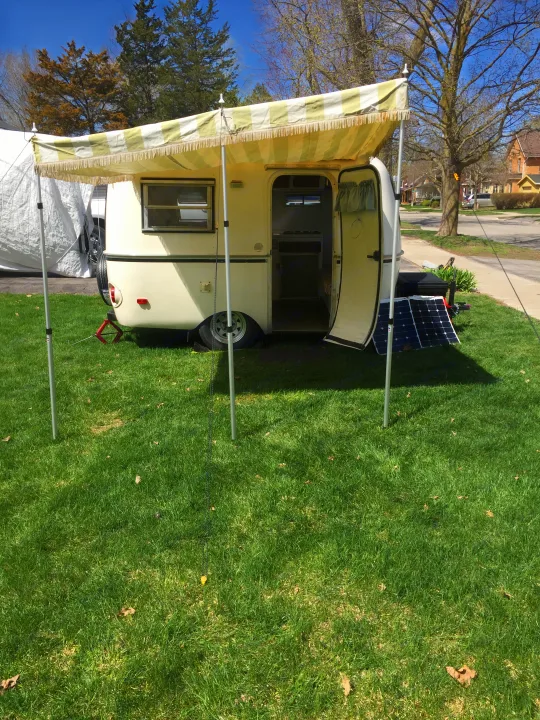 A cream RV with an extended yellow striped awning & solar panel. Parked on grass, ready for an **rv rental** adventure. (Image rotated 90°). Boler B13 1973