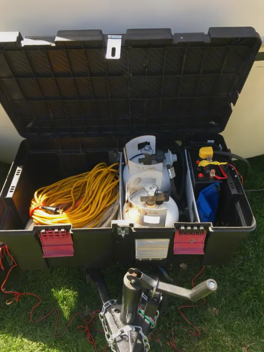 Inside a portable power box for an RV rental: propane tanks, a battery system, and an extension cord near the trailer hitch.. Boler B13 1973