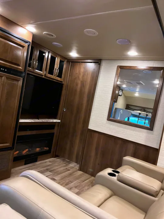 Inside an RV rental: a modern living area with light wood cabinetry, cream recliners, TV, and electric fireplace.. Jayco Greyhawk 2020