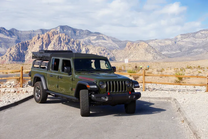 Green Jeep Gladiator with camping gear in desert mountains. An ideal RV rental for outdoor adventures.. Fiat Jeep Gladiator 2023