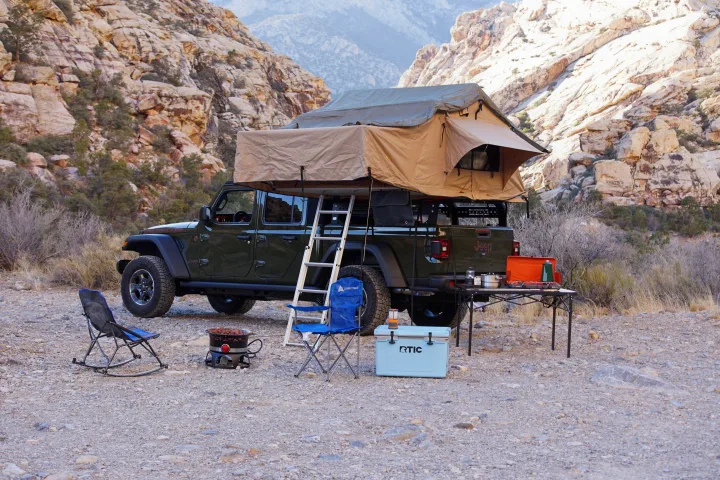 Experience off-grid camping with an RV rental! Jeep Gladiator, rooftop tent, cooler, chairs, and stove in a desert landscape.. Fiat Jeep Gladiator 2023