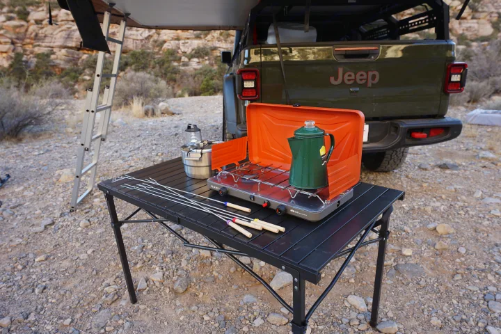 Enjoy an rv rental adventure! Portable stove, coffee pot, and roasting sticks ready on a table for delicious outdoor camping meals.. Fiat Jeep Gladiator 2023