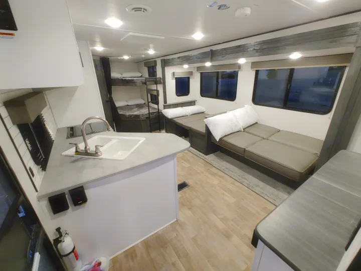 Modern RV rental interior with a compact kitchen, comfy bunk beds, and a convertible dinette/lounge area. Ideal for travel!. Keystone RV Hideout 2022
