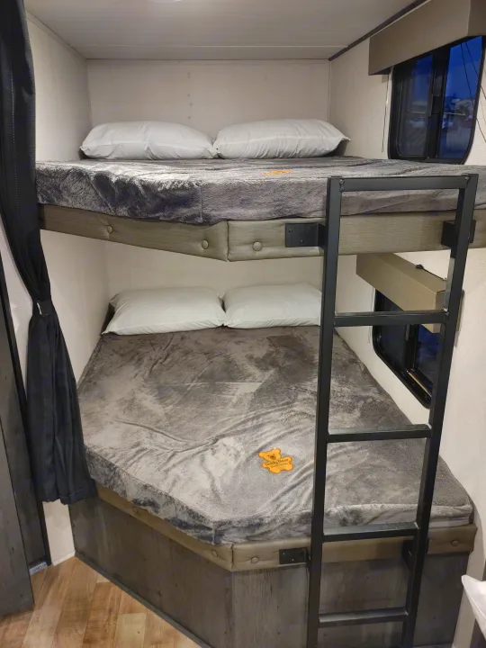 Cozy bunk beds in an rv rental, featuring gray blankets, white pillows, and a ladder for access to the top bunk.. Keystone RV Hideout 2022