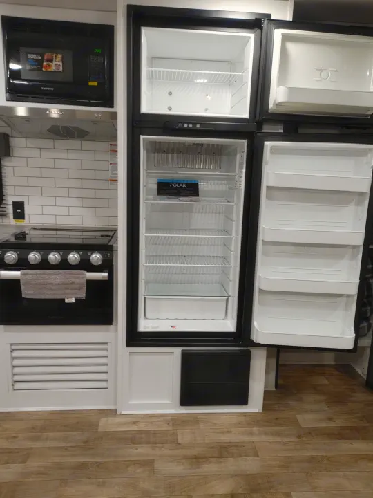 RV rental kitchen appliances: microwave, stove, and a clean, empty, two-door refrigerator with both doors open.. Keystone RV Hideout 2022
